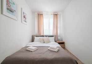 Un letto rifatto con cuscini, un comodino con una lampada e due quadri appesi al muro.