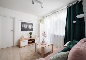 Un soggiorno moderno con un tavolino in legno, un quadro appeso al muro, una pianta in vaso e una tenda verde.