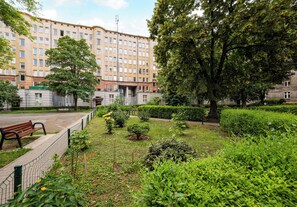 A park with a bench, a fence, and a building in the background. - Żelazna Urban Comfort Apartment (Warszawa)
