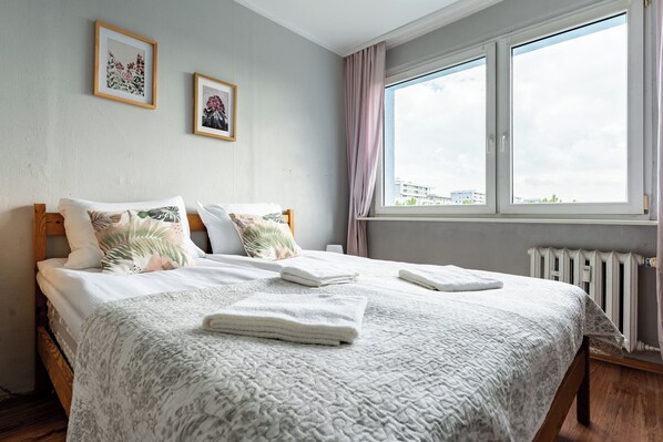 Ein Schlafzimmer mit einem großen Bett, einem Fenster mit Vorhängen und zwei gerahmten Bildern an der Wand.