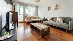Una sala de estar con sofá, mesa de centro, televisor y ventana con cortinas.