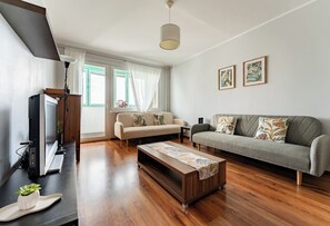 Ein Wohnzimmer mit einer Couch, einem Couchtisch, einem Fernseher und einem Fenster mit Vorhängen.