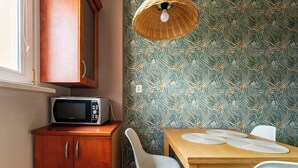 Una cocina con microondas, armarios de madera, una mesa de comedor con sillas y un papel tapiz estampado.