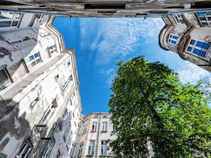 Vista de la esquina de un edificio con un árbol en primer plano, múltiples ventanas y cielo despejado.