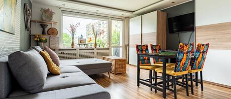 A modern living room with a grey sofa, wooden dining table, and colorful cat-themed chairs.