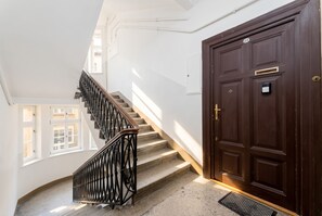 Eine Treppe mit schwarzer Metallreling führt zu einer Empore, dort befindet sich eine dunkle Holztür mit Klingel und ein Fenster mit vielen kleinen Glasscheiben.