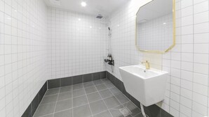 A modern bathroom with white tiled walls, a black-tiled floor, a white sink with a gold faucet, and a shower with a gold-framed mirror. - Gwangju Hotel Lantana - Hanam (Gwangju)