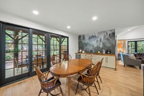 Ein moderner Essbereich mit einem Holztisch und Stühlen, eine Küche mit einem großen Gemälde und Blick durch große Glastüren.