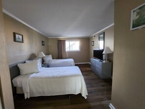 Ein Hotelzimmer mit zwei Betten, einem Schminktisch, einem Fernseher und einem Fenster mit Vorhängen.