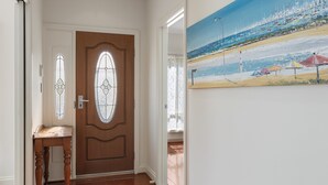 A hallway with a wooden door, a small table, and a painting of a beach scene. - Family-friendly 4-bed Home With Parking (Adelaide)
