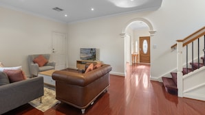 A living room with a sofa, armchair, and coffee table, a staircase, and a hallway leading to a door. - Family-friendly 4-bed Home With Parking (Adelaide)