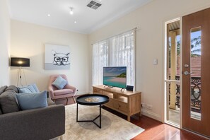 A living room with a sofa, a small table, a TV, and a door leading to an outdoor area. - Family-friendly 4-bed Home With Parking (Adelaide)