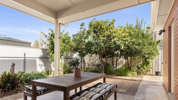 A covered patio area with a wooden table and bench, surrounded by potted plants and a brick wall. - Family-friendly 4-bed Home With Parking (Adelaide)