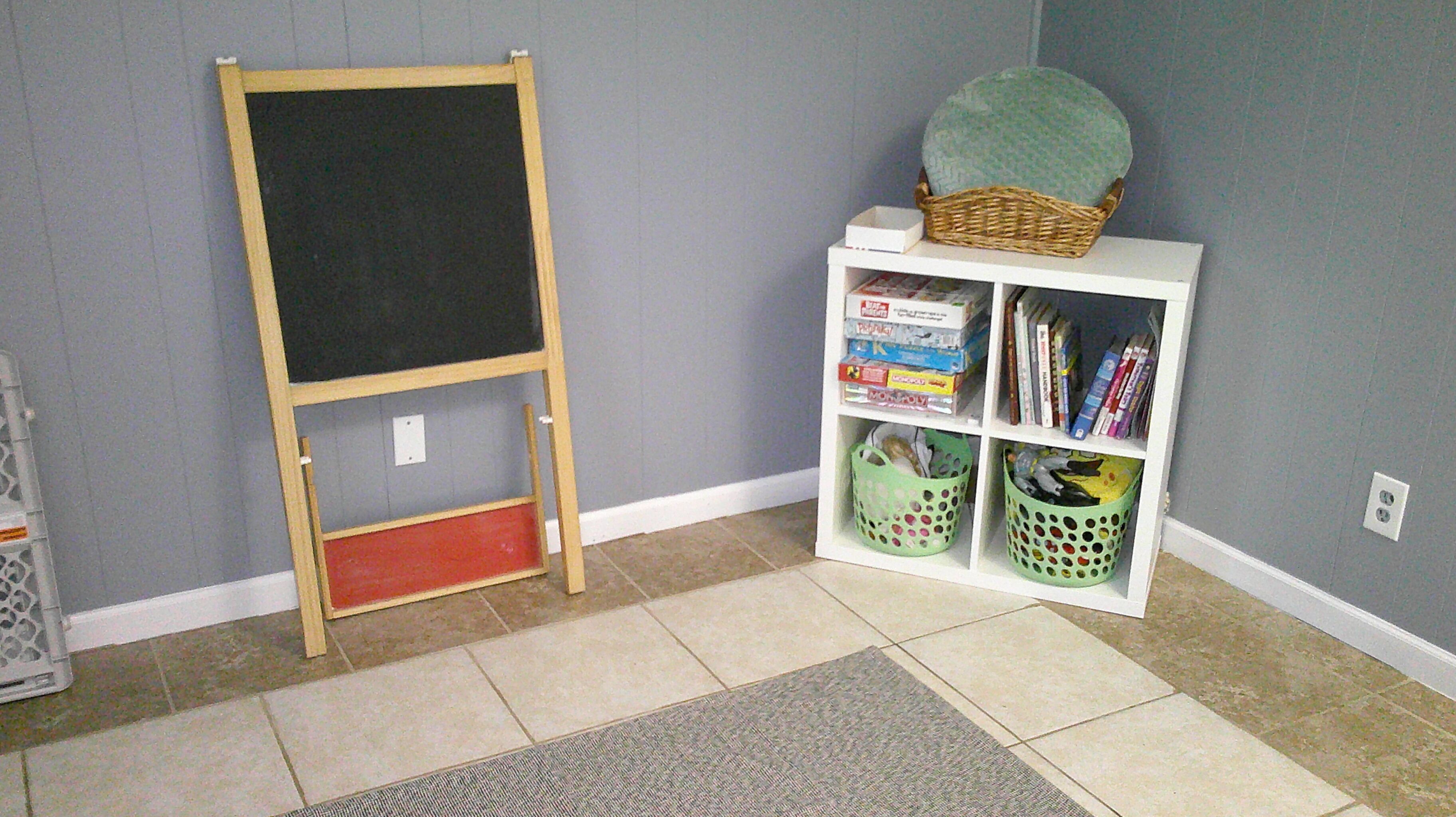 A room with a chalkboard, a bookshelf, and a mat on the floor.