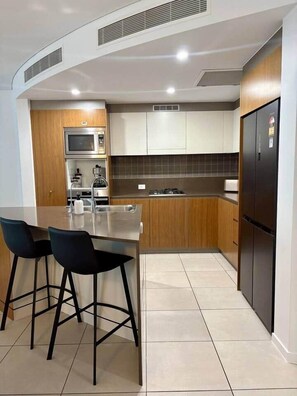 Eine moderne Küche mit Kochinsel, Barhocker, Backofen und Kühlschrank.