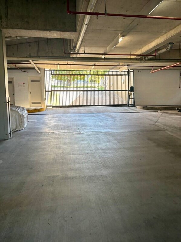 Un espacio interior amplio con piso de concreto, una reja metálica y una puerta a la izquierda.