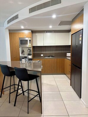 Una cocina moderna con una isla central, taburetes de bar, microondas integrado y un refrigerador.