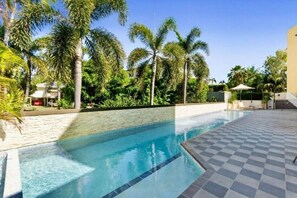 Una piscina con piso a cuadros, rodeada de palmeras y un cielo despejado.