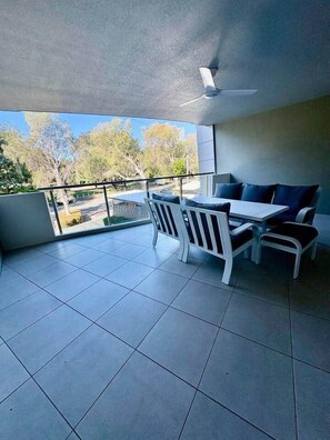 Ein Balkon mit Tisch und Stühlen, einem Deckenventilator und Blick auf Bäume und eine Straße.