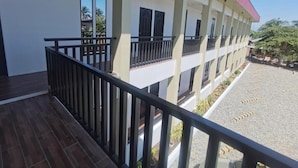 Un edificio con un balcón cubierto, un patio de grava y un tejado rojo.