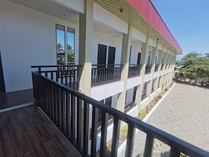 Un edificio con un balcón cubierto, un patio de grava y un tejado rojo.