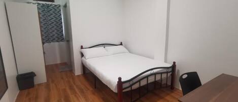 A room with a single bed, a wooden floor, a desk, and a chair.