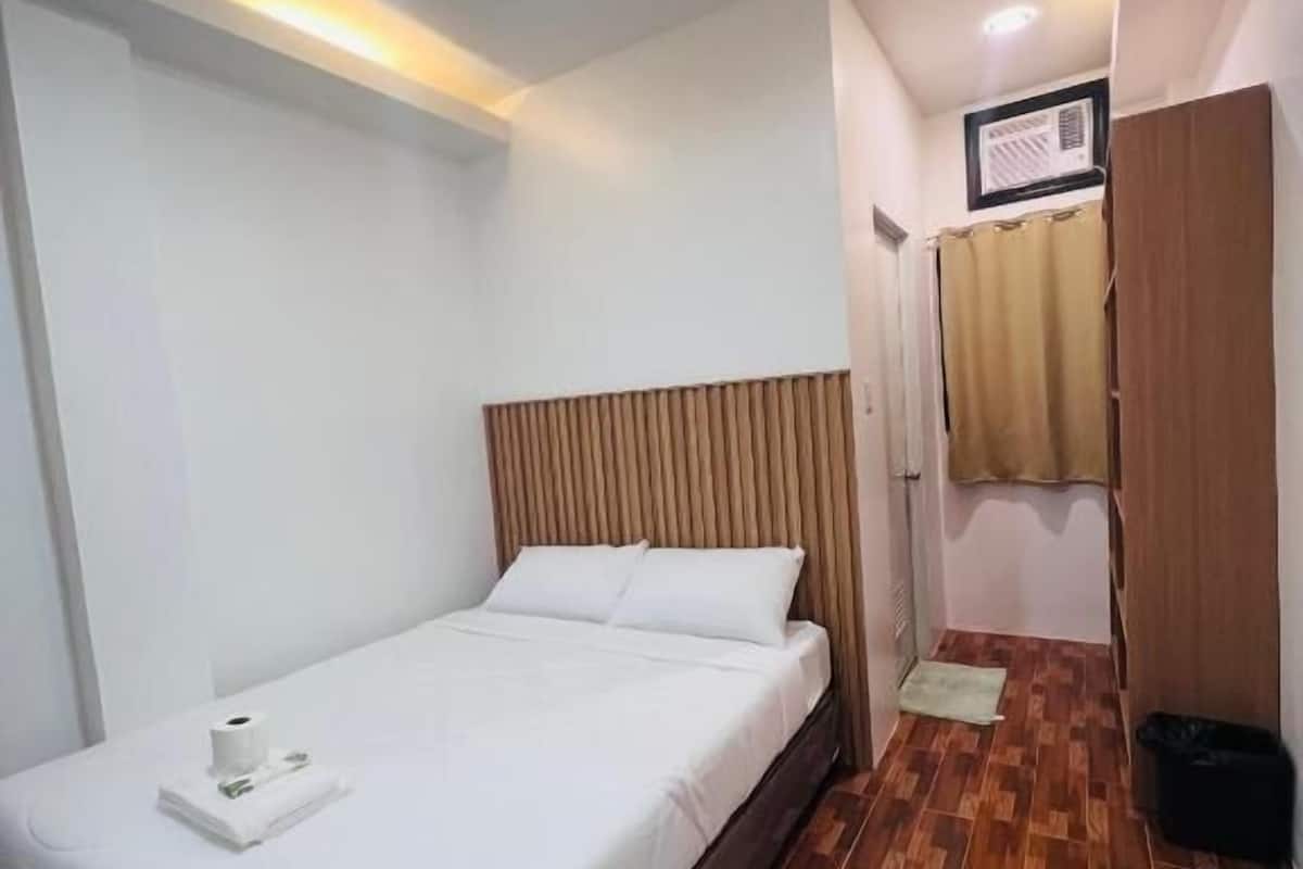 Une chambre d’hôtel avec un lit, un plancher en bois, un luminaire au plafond et une fenêtre avec des rideaux.