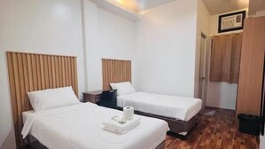 Una habitación de hotel con dos camas, piso de madera y una lámpara en el techo.