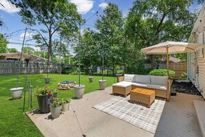 Un patio trasero con mobiliario exterior, una pérgola con luces colgantes y un césped cuidado.