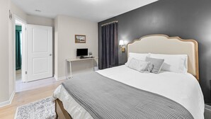A bedroom with a bed, bedside table, lamp, and a door leading to another room. - Walk to Martin City + Sleeps 6 + Yard + Fire Pit (Kansas City)
