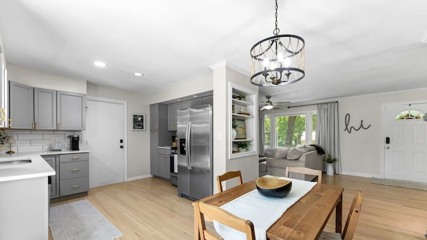 A modern kitchen with grey cabinets, a stainless steel refrigerator, and a dining area with a wooden table and chairs. - Walk to Martin City + Sleeps 6 + Yard + Fire Pit (Kansas City)