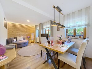 Ein modernes Wohnzimmer mit einer Couch, einem Esstisch mit Stühlen, einem Fernseher und einer Ziegelwand.
