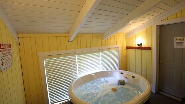 Ein Whirlpool in einem Raum mit gelben Wänden, einem Fenster mit Jalousien und einer Tür mit Ausgangsschild.