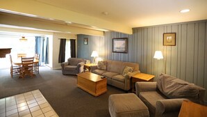 Ein Wohnzimmer mit einer Couch, Sesseln, einem Couchtisch, einem Esstisch mit Stühlen und Lampen.