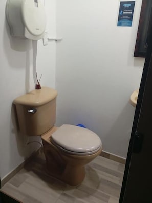 Un baño pequeño con inodoro, secador de manos y un cubo de basura azul.