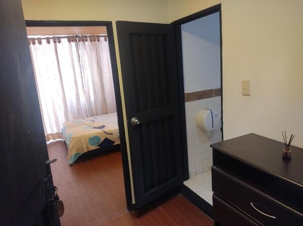 A room with a bed, a door, a small table with a bottle, and a wall-mounted dispenser. - Hotel Rico Campo (Armenia)