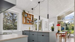 A modern kitchen with a central island, wooden shelves, and a dining area with a table and chairs. - 4 Star Holiday Home in Storvorde (Storvorde)