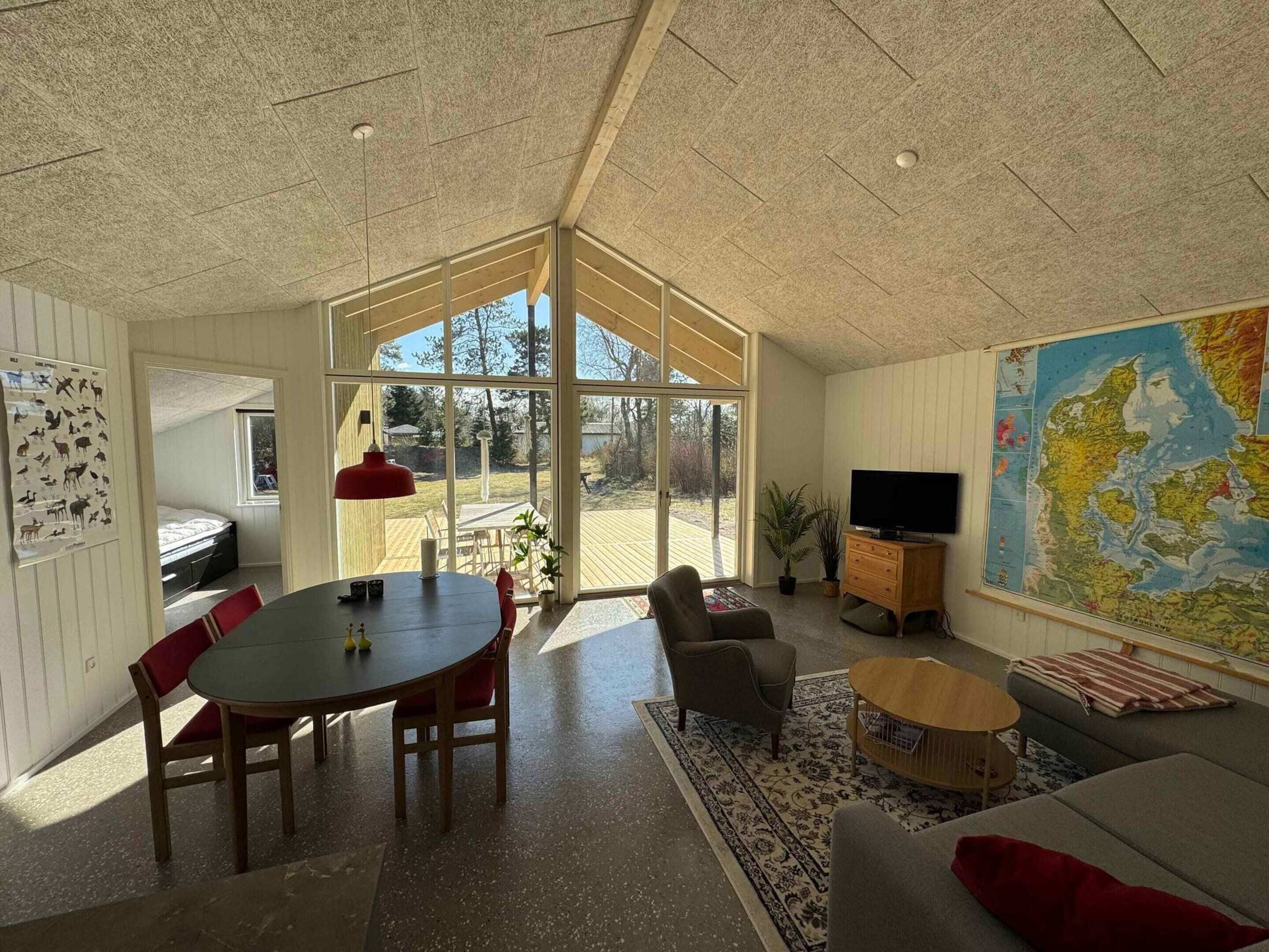 Et rummeligt værelse med et stort vindue, et spisebord, en sofa, et fjernsyn og et kort på væggen.
