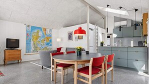 A modern kitchen with grey cabinets, a dining area with a round table and red chairs, a large map on the wall, and a TV on a wooden cabinet. - 4 Star Holiday Home in Storvorde (Storvorde)