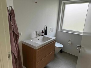 A bathroom with a white sink, wooden vanity, a toilet, and a window. - 4 Star Holiday Home in Storvorde (Storvorde)