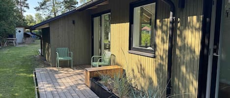 Un bâtiment en bois doté d’une terrasse, de deux chaises et d’une fenêtre.