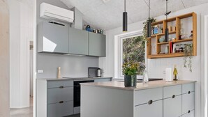 A modern kitchen with grey cabinetry, a central island, a built-in oven, and a window with a view of greenery. - 4 Star Holiday Home in Storvorde (Storvorde)