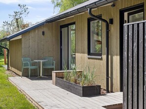 A wooden cabin with a deck, two chairs, a table, and a planter with plants. - 4 Star Holiday Home in Storvorde (Storvorde)