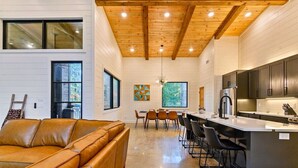 A modern kitchen with a central island, wooden ceiling beams, and a dining area with chairs. - NEW! Heated Pool, Hot Tub, Outdoor Lounge, Games (Broken Bow)
