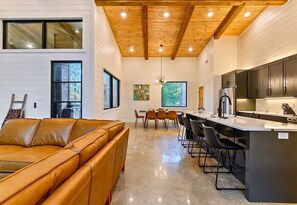 A modern kitchen with a central island, wooden ceiling beams, and a dining area with chairs. - NEW! Heated Pool, Hot Tub, Outdoor Lounge, Games (Broken Bow)