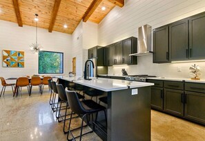 A modern kitchen with a central island, dark cabinets, and a wooden ceiling. - NEW! Heated Pool, Hot Tub, Outdoor Lounge, Games (Broken Bow)