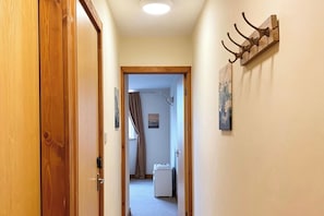 Un passadís amb una porta de fusta, un penjador i una habitació petita amb finestra i un radiador.
