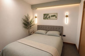Un dormitori amb llit, una tauleta de nit, una làmpada penjada a la paret i una planta.