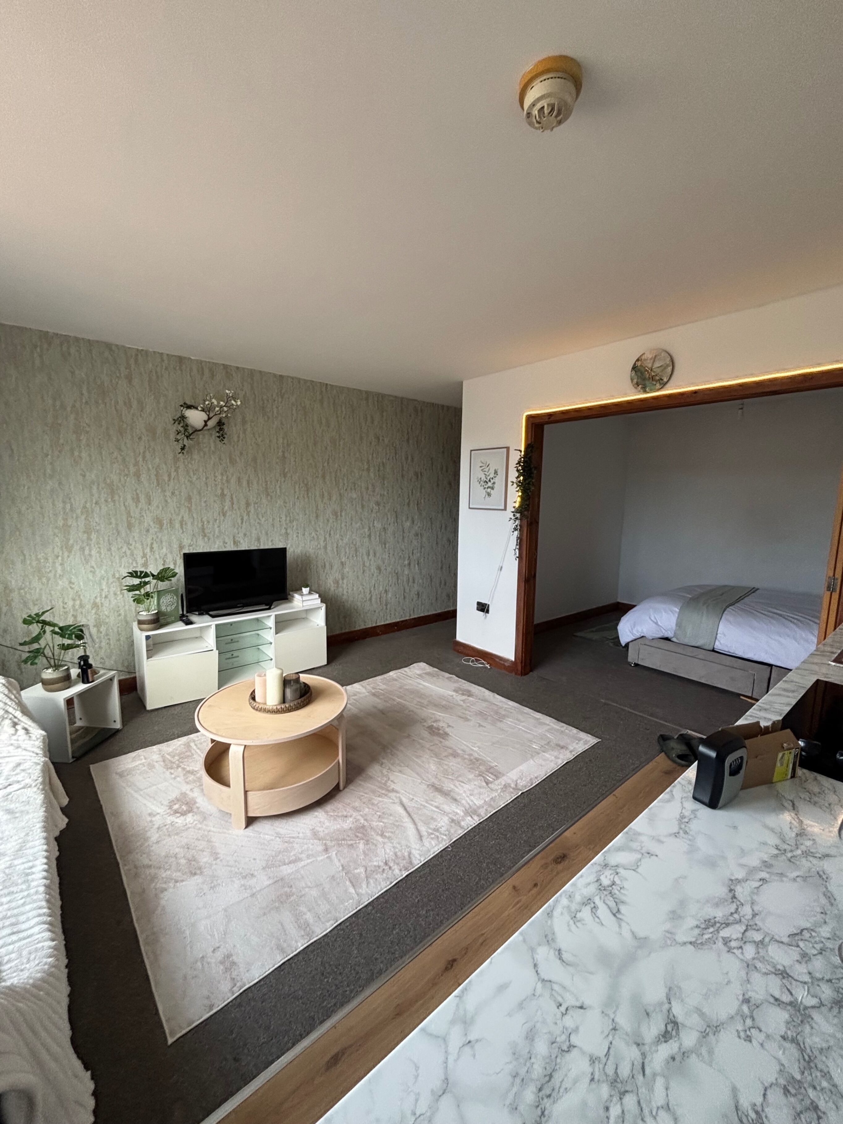 A modern bedroom with a bed, a TV, a desk, and a small round table.