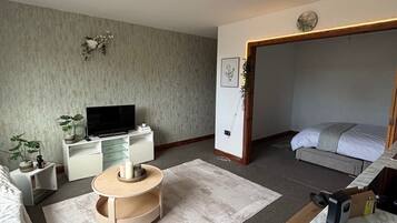 A modern bedroom with a bed, a TV, a desk, and a small round table.